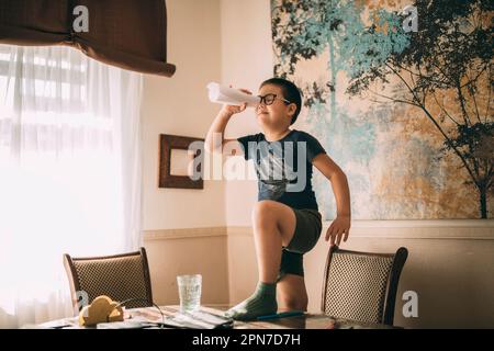 Ein kleiner Schüler stand mit dem Fuß auf dem Tisch wie ein Pirat mit einem Teleskop. Stockfoto