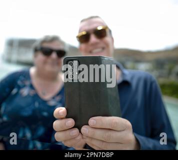 Frau und Mann lächeln, draußen, schauen auf Handydisplay, Bokeh Stockfoto