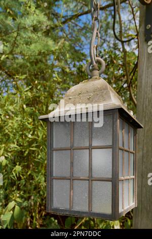 Die Laterne wurde bei Tageslicht ausgeschaltet, an einer Holzplanke befestigt und von Vegetation umgeben Stockfoto