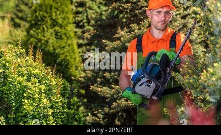 Professioneller, Kaukasischer Landschaftspfleger, Der Saisonale Gartenwartung Mit Einer Elektrischen Heckenschere Durchführt. Thema Gartengeräte. Stockfoto