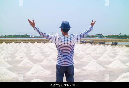 Mann mit ausgestreckten Armen bis zur weitläufigen Salzpfanne in der Erntesaison, Samut Sakhon Provinz in Thailand Stockfoto