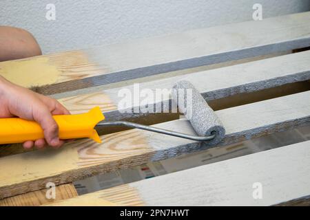 Lackieren und Färben mit weißer Holzoberfläche mit Malerwalze, Nahaufnahme Stockfoto