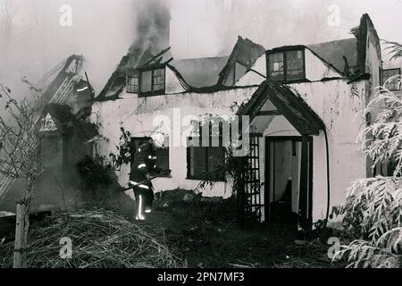 Feuerwehrleute dämpfen ein Feuer in einer abgelegenen Strohhütte in der Nähe von Salisbury 1990. Stockfoto