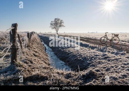 Felder bedeckt mit Heiserfrost und ein Fahrrad, das an einem sonnigen Wintermorgen auf einer Landstraße steht. Landschaftslandschaft. Stockfoto