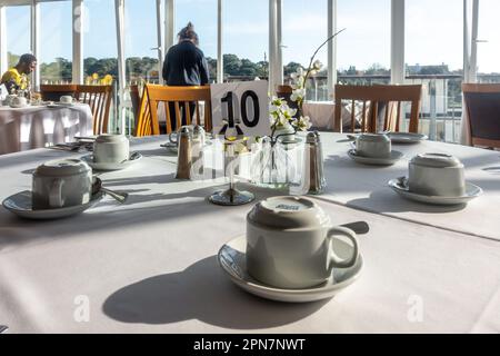 Tisch 10 in einem Hotelrestaurant mit sauberer Tischdecke und Tassen und Untertassen, die für Gäste zum Frühstück bereit stehen. Stockfoto