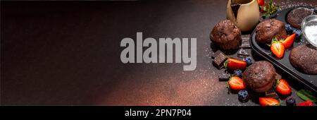 Schokoladen-Muffins mit Beeren. Muffin-Pfanne mit hausgemachten süßen, dunklen Schokoladen-Cupcakes mit Kakaosoße, Zuckerpulver und frischen Erdbeeren, Blaubeeren Stockfoto