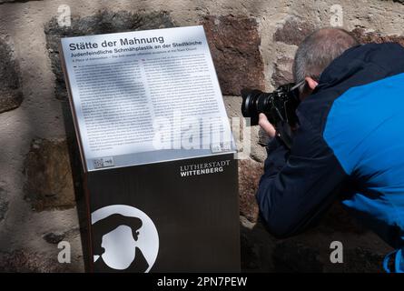 17. April 2023, Sachsen-Anhalt, Lutherstadt Wittenberg: Ein neuer Text ist auf einer Informationstafel unter der als Judensau bekannten eindrucksvollen Skulptur der Stadtkirche in Wittenberg zu sehen. Die Erleichterung ist höchst umstritten. Jetzt enthält der neue Text Informationen über den Ort der Ermahnung. Im vergangenen Jahr hatte der gemeinderat der Gemeinde Stadtkirche angekündigt, dass er sich mit der weiteren Entwicklung des „Ermahnungsgeländes“ an der Stadtkirche St. Marien befassen werde. Gleichzeitig entwickelte die Protestantische Akademie Rollups, die die Probleme des kirchlichen Antijudaismus und, s aufzeigten Stockfoto