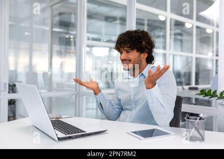 Verärgerter junger Geschäftsmann, der im Büro mit einem Laptop arbeitet, Mann kann technisches Projekt nicht rechtzeitig abschließen, hispanischer Mann frustriert am Schreibtisch zu sitzen. Stockfoto