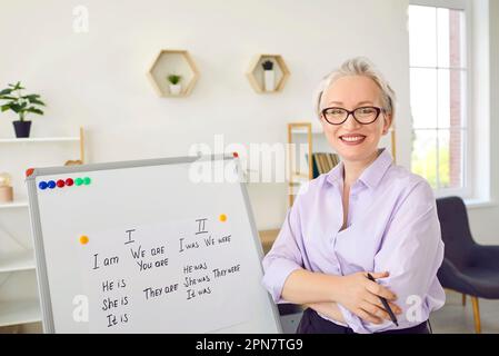 Eine glückliche, lächelnde Englischlehrerin, die im Klassenzimmer am Whiteboard steht Stockfoto