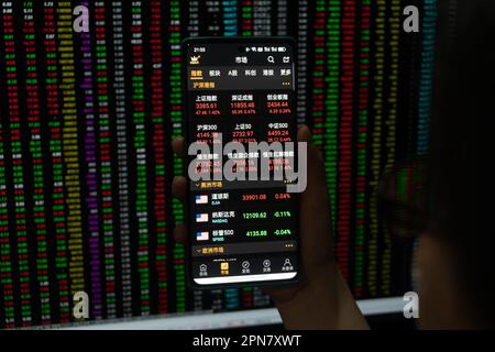 SHANGHAI, CHINA - 17. APRIL 2023 - Ein Aktieninvestor überprüft den Aktienindex auf seinem Handy und Computer am Ende des Tages in Shanghai, Stockfoto