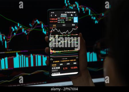 SHANGHAI, CHINA - 17. APRIL 2023 - Ein Aktieninvestor überprüft den Aktienindex auf seinem Handy und Computer am Ende des Tages in Shanghai, Stockfoto