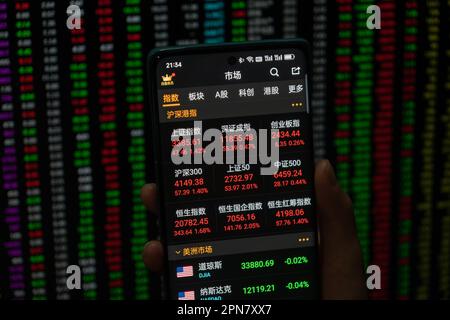 SHANGHAI, CHINA - 17. APRIL 2023 - Ein Aktieninvestor überprüft den Aktienindex auf seinem Handy und Computer am Ende des Tages in Shanghai, Stockfoto