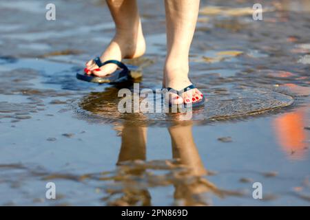 Eine Frau mit Flip-Flop, die am Ufer eines Meeresstrands spaziert. Vung Tau. Vietnam. Stockfoto