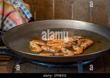 Garnelen bei geringer Hitze in einer Paella-Pfanne zubereiten, um eine Fideua und Paella mit Meeresfrüchten zuzubereiten Stockfoto