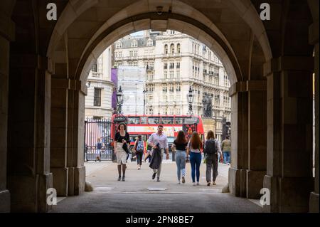 LONDON - 18. Mai 2022: Eine geschäftige Londoner Szene, während die Menschen durch den Eingangsbogen zur Horse Guards Parade gehen, mit dem berühmten roten Doppeldeckerbus in t Stockfoto