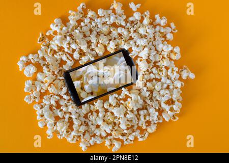 Smartphone und Popcorn auf dem gelben Tisch. Technologiekonzept. Kino auf einem Smartphone mit Popcorn-Hintergrund Stockfoto