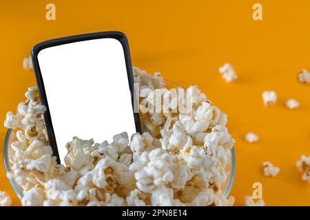 Handy und Popcorn in einer Schüssel, auf einem gelben Tisch, Nahaufnahme. Technologiekonzept Stockfoto