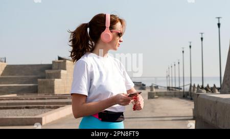 Sportlerin schaut Cardio, Fitness in der Stadt. Die Frau schaut sich die Kalorien beim Training an. Übung auf der Straße. Gesunder Lebensstil. Stockfoto