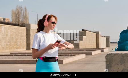 Sportlerin schaut Cardio, Fitness in der Stadt. Die Frau schaut sich die Kalorien beim Training an. Übung auf der Straße. Gesunder Lebensstil. Stockfoto