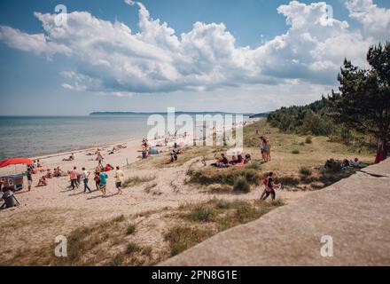 Eine malerische Strandszene mit einer großen Menschenmenge, die das warme Sommerwetter und das glitzernde Meer im Hintergrund genießen Stockfoto