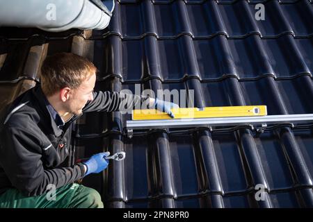 Handwerker, der eine Wasserwaage auf einer Montageschiene für Solarmodule verwendet Stockfoto