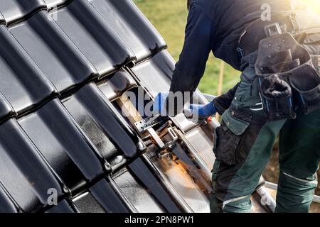 Handwerker, der eine Halterung für ein Sonnenkollektormontagesystem auf einem Dach befestigt Stockfoto