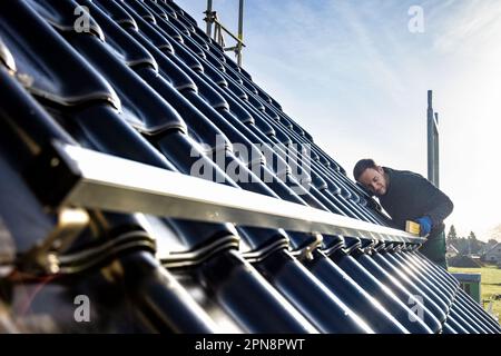 Ein Handwerker, der eine Montageschiene für Solarmodule auf dem Dach eines Einfamilienhauses installiert Stockfoto