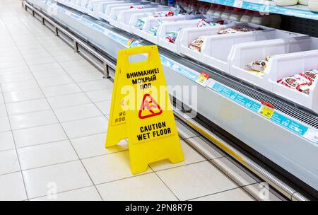 Samara, Russland - 5. Juni 2022: Vorsicht nasser Boden gelbes Warnschild auf einem Fliesenboden in einem Supermarkt vor dem Hintergrund von verschwommenen Produkten auf dem Stockfoto