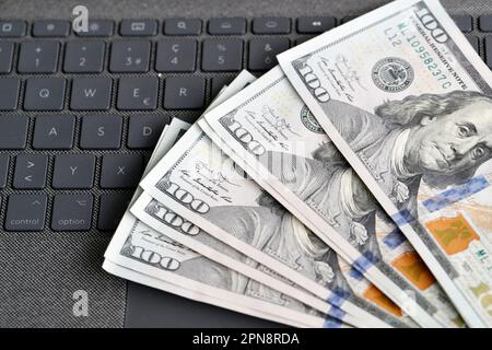 Geld und Religion. Banknoten von US-Dollar mit Rosenkranz auf einem Laptop. Katholisches Finanz-, Ökonomie- und Glaubenskonzept. Stockfoto