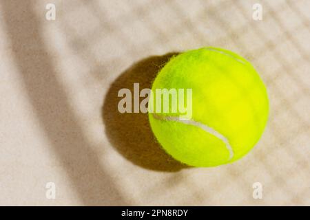 Gelber Tennisball am Sandstrand mit Schlägerschatten Stockfoto