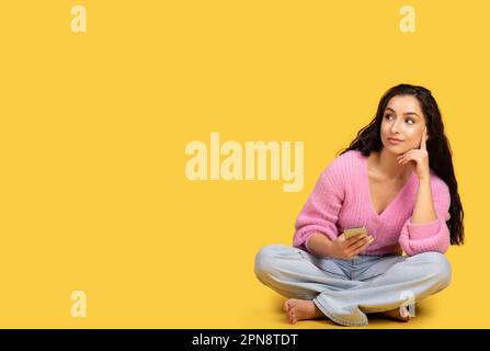 Die rücksichtsvolle barfuß-Dame der Millennials mit Smartphone sitzt auf dem Boden und schaut auf den Kopierbereich Stockfoto