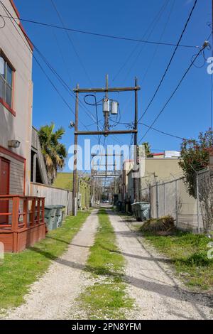 Galveston, Texas, USA - Februar 2023: Unbefestigte Straße mit Stromleitungen zwischen den hinteren Gebäuden in der Nähe des Stadtzentrums Stockfoto
