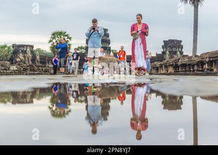 SIEM REAP, KAMBODSCHA - 11. JANUAR 2023: Touristen fotografieren einen frechen Makaken-Affen, der eine Banane isst, die er gerade einem Touristen gestohlen hat Stockfoto