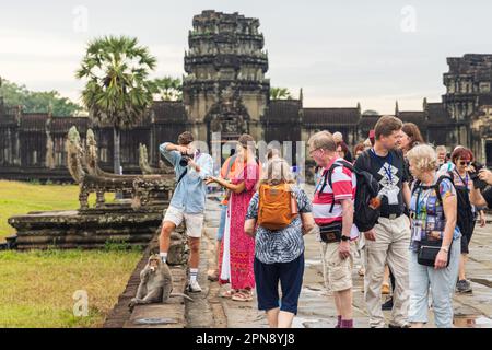 SIEM REAP, KAMBODSCHA - 11. JANUAR 2023: Touristen fotografieren einen frechen Makaken-Affen, der eine Banane isst, die er gerade einem Touristen gestohlen hat Stockfoto