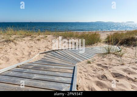 Holzsteg führt an einem sonnigen Tag im Sommer zu einem leeren Strand in Hanko, Finnland. Stockfoto