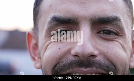 Ein junger Mann aus dem Nahen Osten nähert sich seinem Gesicht und lächelt vor der Kamera. Ein arabischer 20s-Mann mit Falten Stockfoto