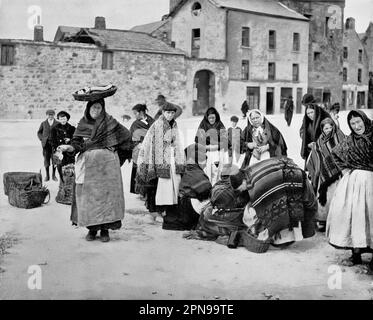 Ein Blick aus dem späten 19. Jahrhundert auf den Fischmarkt in der Nähe eines der alten Stadttore in Galway City, Irland. Die älteren Frauen und ein oder zwei jüngere Mädchen sind Claddagh-Leute, die den neu gefangenen Hering verkaufen, für den die Küste von Galway berühmt ist. Stockfoto