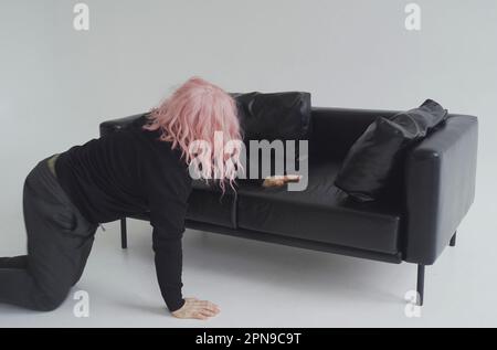 Ein betrunkener Mann in einer rosa Perücke kriecht über den Boden zum Sofa, schläft auf dem Sofa. Stockfoto