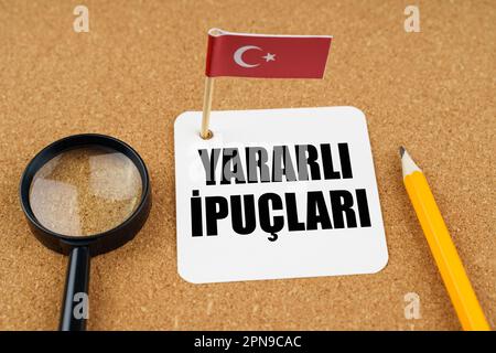 Auf dem Tisch liegt die Flagge der Türkei, ein Bleistift, eine Lupe und ein Blatt Papier mit einer ins Englische übersetzten Inschrift in Türkisch - hilfreich Stockfoto