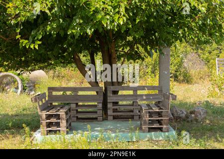 Palettentisch und Stühle stehen im Garten unter einem Baum, Palettenmöbel, Handroboter Stockfoto