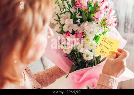 Alles Gute Zum Muttertag. Seniorin liest Grußkarte, die in einem Blumenstrauß zu Hause gefunden wurde. Überraschungsgeschenk für die Frühjahrsferien. Nahaufnahme von oben von n Stockfoto