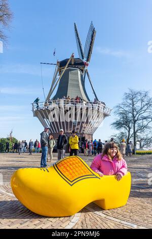 Ein junges Mädchen, das sich in einem Riesenclog bei der Mühle, den Gartenanlagen des Keukenhof, Lisse, Südholland (Zuid-Holland), Königreich der Niederlande, aufstellt Stockfoto