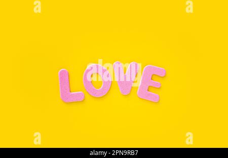 Liebe. Pinkfarbene Buchstaben mit dem Wort „Liebe“ auf gelbem Hintergrund. Das Konzept des Valentinstages. Liebeswort mit pinkfarbenen Buchstaben auf einem gelben Stockfoto