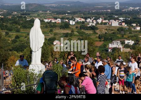 Statue der Jungfrau Maria, Königin des Friedens, auf dem Berg Podbrdo, umgeben von betenden Pilgern. Stockfoto