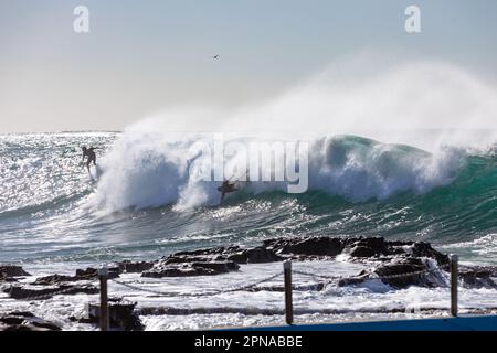 Wellen stürzen über Dee Why Beach Rockpools, Ozeanschwimmbecken. Zwei Surfer in großen Wellen. Stockfoto