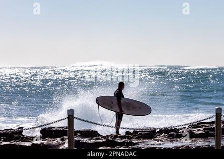 Wellen stürzen über Dee Why Beach Rockpools, Ozeanschwimmbecken. Der Surfer wartet darauf, in die Wellen zu kommen Stockfoto