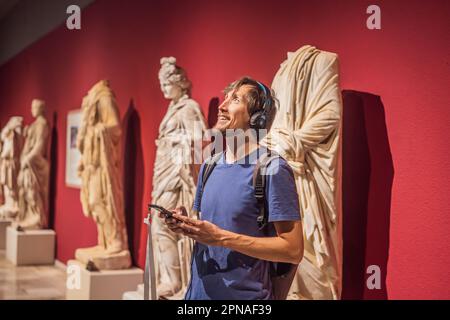 Porträt eines zeitgenössischen Mannes, der sich Skulpturen ansieht und Audioguide auf der Museumsausstellung hört Stockfoto