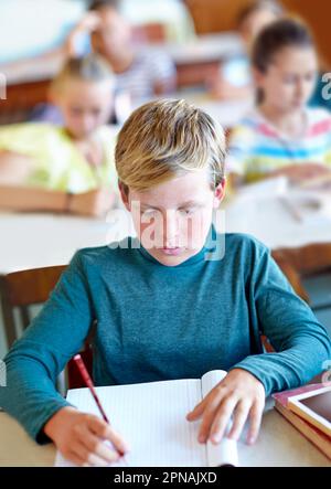 Er ist ein fleißiger Schüler. Ein Junge, der im Unterricht in sein Notizbuch schreibt. Stockfoto