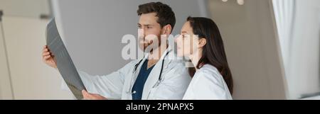 Zwei Ärzte sehen und diskutieren in Uniform eine Röntgen- oder MRT-Untersuchung der Wirbelsäule des Patienten Stockfoto