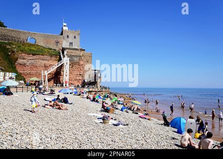 Touristen entspannen sich am Jacobs Ladder Beach mit dem Schloss auf dem Hügel, Sidmouth, Devon, Großbritannien, Europa. Stockfoto